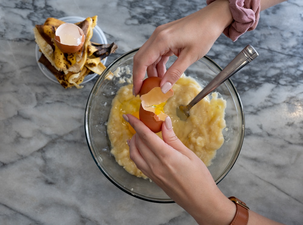 Egg being cracked into banana bread mix